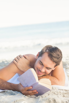 微笑英俊的男人在海滩上看书