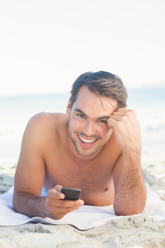 趴在海滩上拿着手机的男人