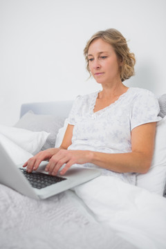金发女子坐在床上使用笔记本电脑
