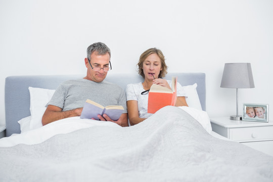 快乐的一对夫妇坐在床上看书