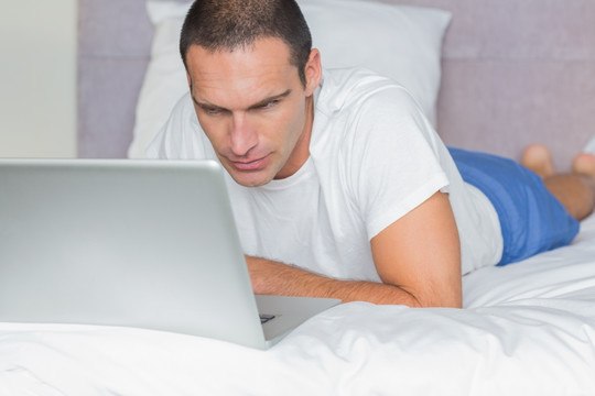男人趴在床上使用笔记本电脑