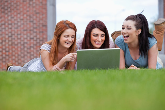 在草坪上使用笔记本电脑的女学生