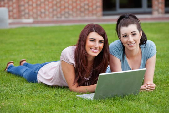 趴在草坪上用电脑的两个女学生