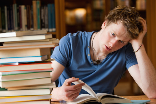 皱眉的男学生在图书馆里读一本书