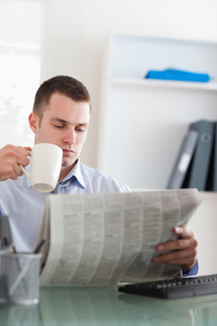 年轻的商人在看报纸喝咖啡