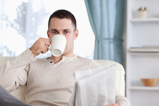 男子手拿报纸在客厅里喝茶