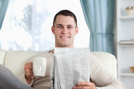 男人坐沙发上手拿报纸和杯子
