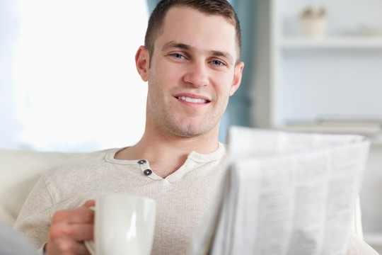 男人坐沙发上手拿报纸和杯子