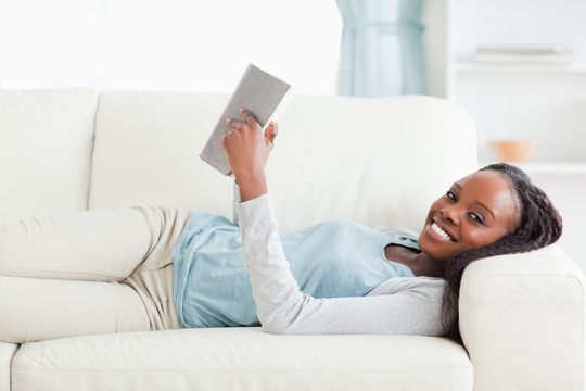 微笑的女人躺在沙发上看书