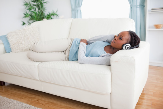 年轻女子躺在沙发上听音乐