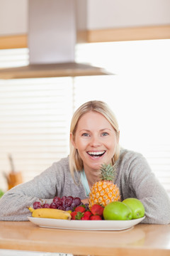快乐的笑女人坐在盘子后面的水果