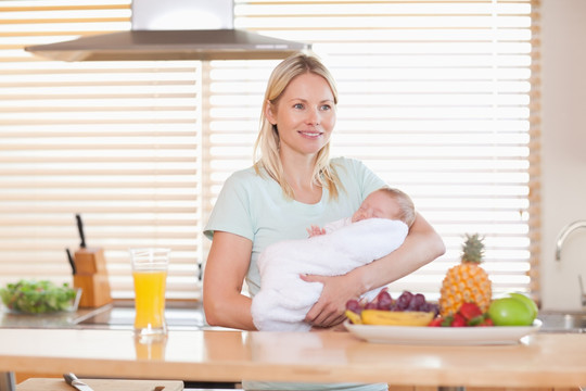 年轻的女人在厨房里抱着婴儿