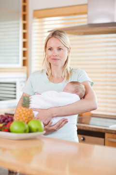 年轻的女人在厨房里抱着婴儿