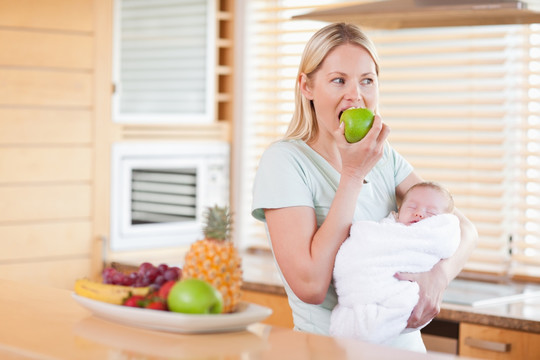 在厨房抱着婴儿吃苹果的女人