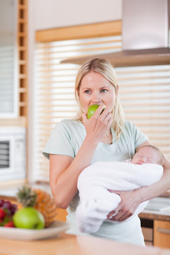 在厨房抱着婴儿吃苹果的女人