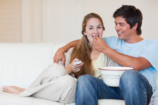 年轻的夫妇边吃爆米花边看电视