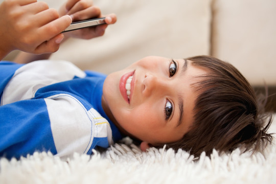 小男孩躺在地毯上用手机