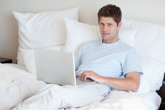 躺在床上的男子使用笔记本电脑
