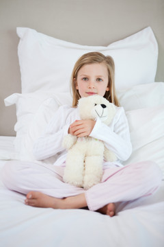 小女孩在床上抱着她的泰迪熊