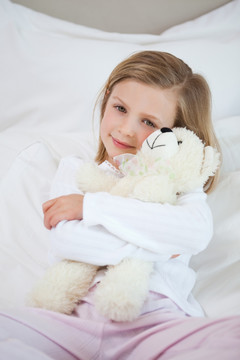 小女孩在床上抱着她的泰迪熊