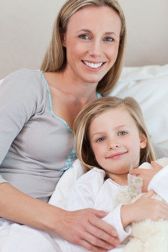 面带微笑的母亲抱着女儿在床上
