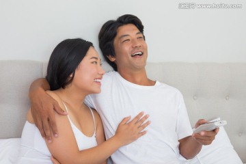 夫妇坐在床上微笑着看着电视