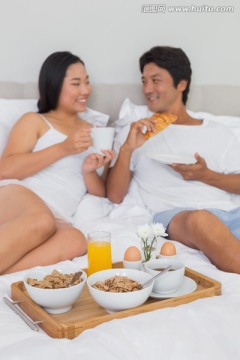 夫妇躺在床上微笑着吃着早餐