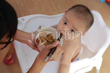 妈妈给坐在餐桌餐椅的胖儿子喂饭