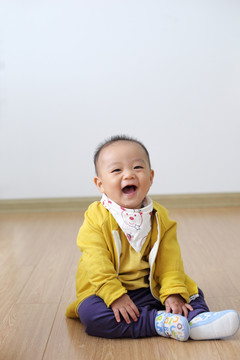 打扮时尚的婴儿坐在仿木地板上笑