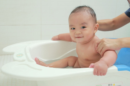 妈妈扶着坐着洗澡盆里胖胖婴儿
