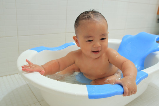 胖胖婴儿坐洗澡盆里双手扶着盆沿