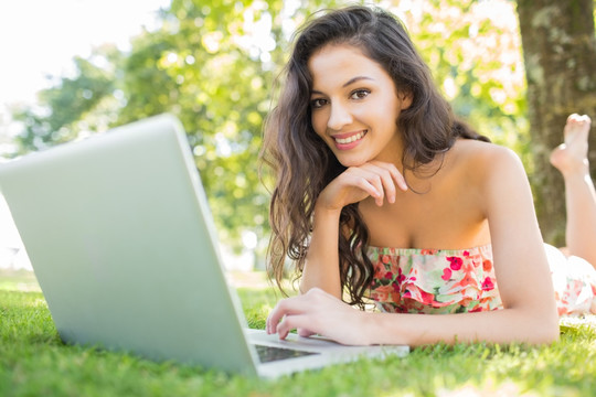 趴在草坪上使用笔记本电脑的女人