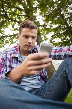 坐在草坪上看手机短信的男学生