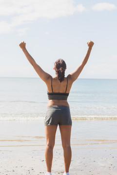 年轻女子举起她的双臂站在海滩上