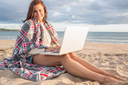 坐在沙滩上用笔记本电脑的女人