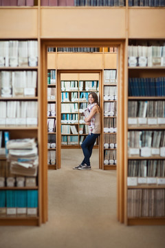 抱着一堆书站在图书馆里的大学生