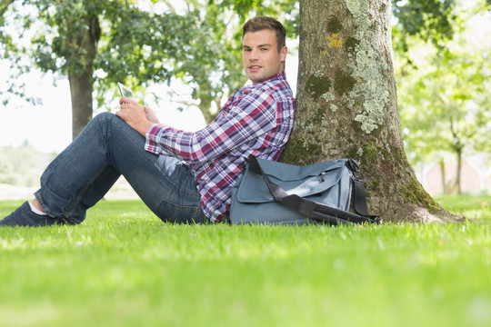 坐在树下用平板电脑的男大学生