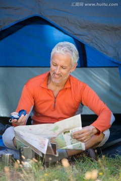 坐在帐篷里看地图和指南针的男人
