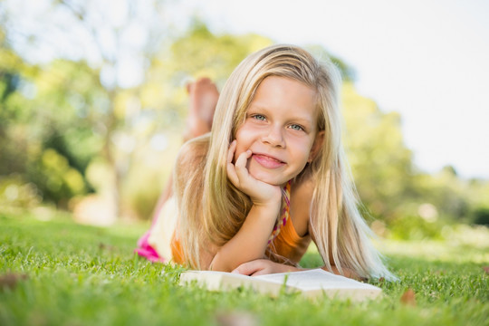 年轻的女孩趴在草地上看书