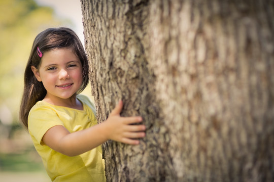 微笑的女孩拥抱着树干