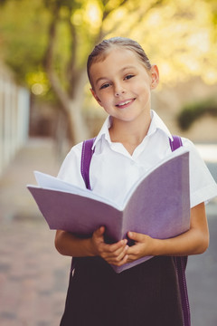 微笑的女学生拿着书本站在校园里