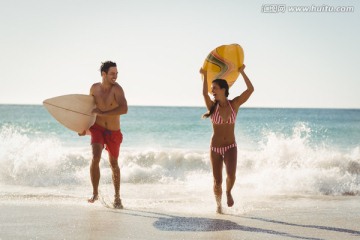 拿着冲浪板在海边奔跑的夫妇