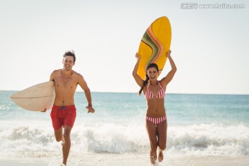 拿着冲浪板在海边奔跑的夫妇