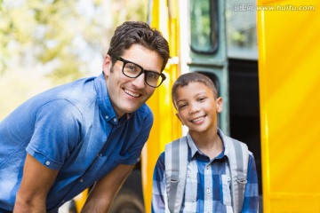 微笑的老师和男学生站在校车外