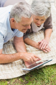 趴在草坪上用平板电脑的老夫妇