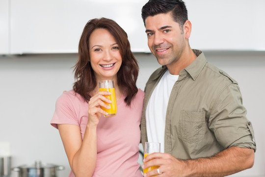 微笑一对夫妇在厨房里喝橙汁