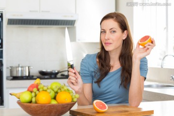 在厨房里拿着一把刀和水果的女人