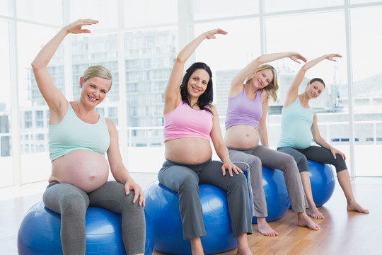 坐在健身球上伸展手臂的孕妇们