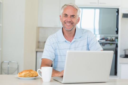 在厨房吃早餐用笔记本电脑的男人