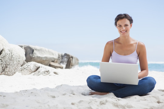 坐在沙滩上用笔记本电脑的女人